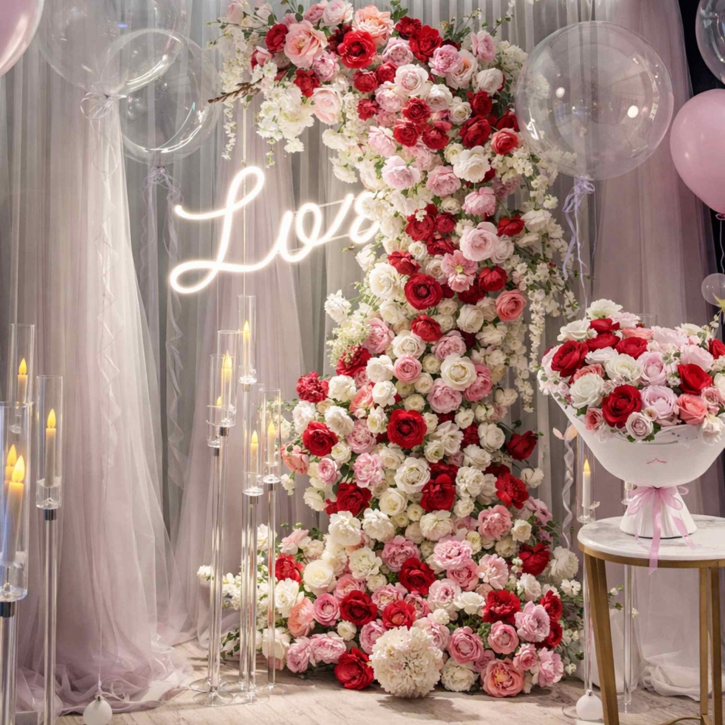Decorative floral arch with red, pink, and white flowers, illuminated by a 'Love' sign, surrounded by balloons and candles.
