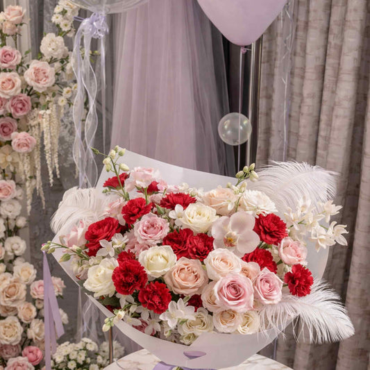 Bouquet of red, pink, and white flowers with decorative feathers on a table.