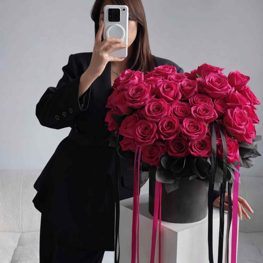 Person holding a large bouquet of pink roses with black ribbons in a minimalistic setting.